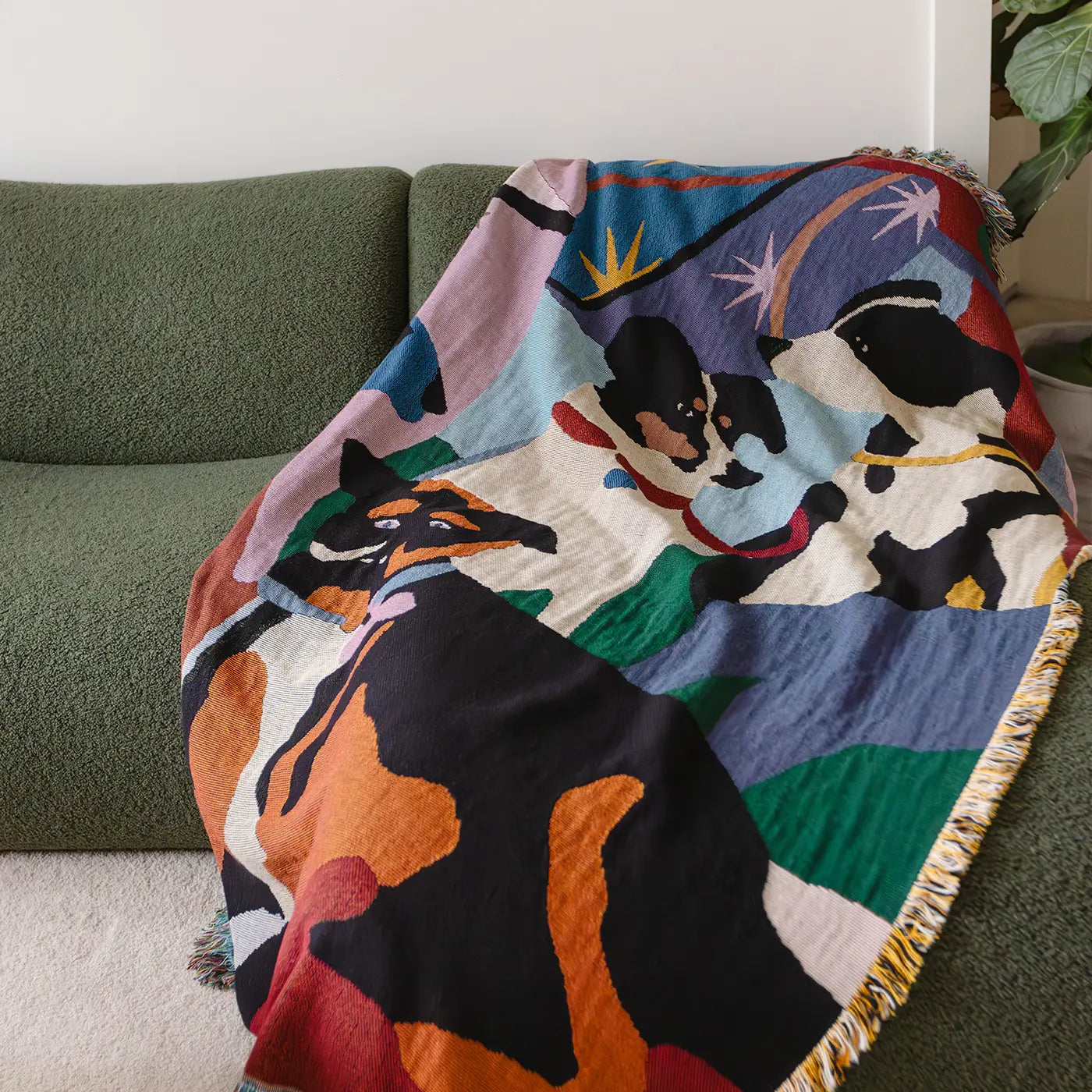 Colorful blanket with dog design draped over a green couch.