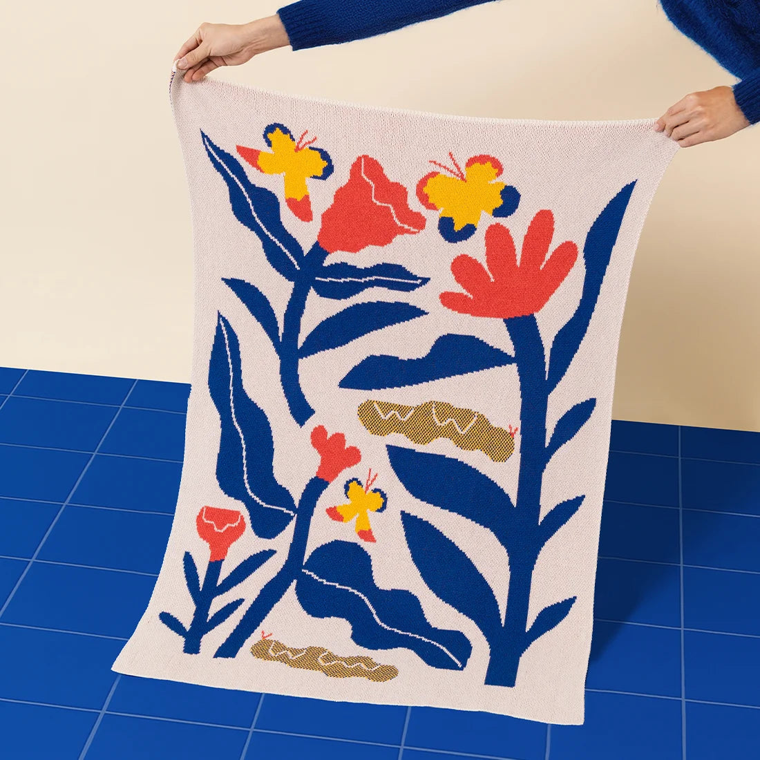 Person holding the Papillons kids blanket on a blue tiled floor.
