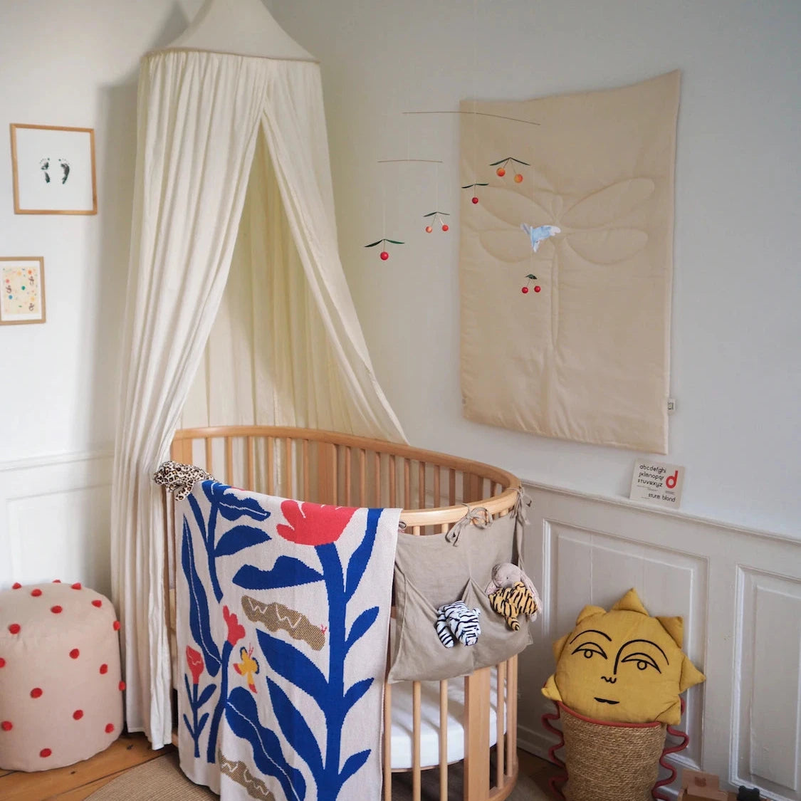 Nursery room with a crib, decorative blanket, and wall art. A baby blanket with flower and butterfly design hangs over the cot. 