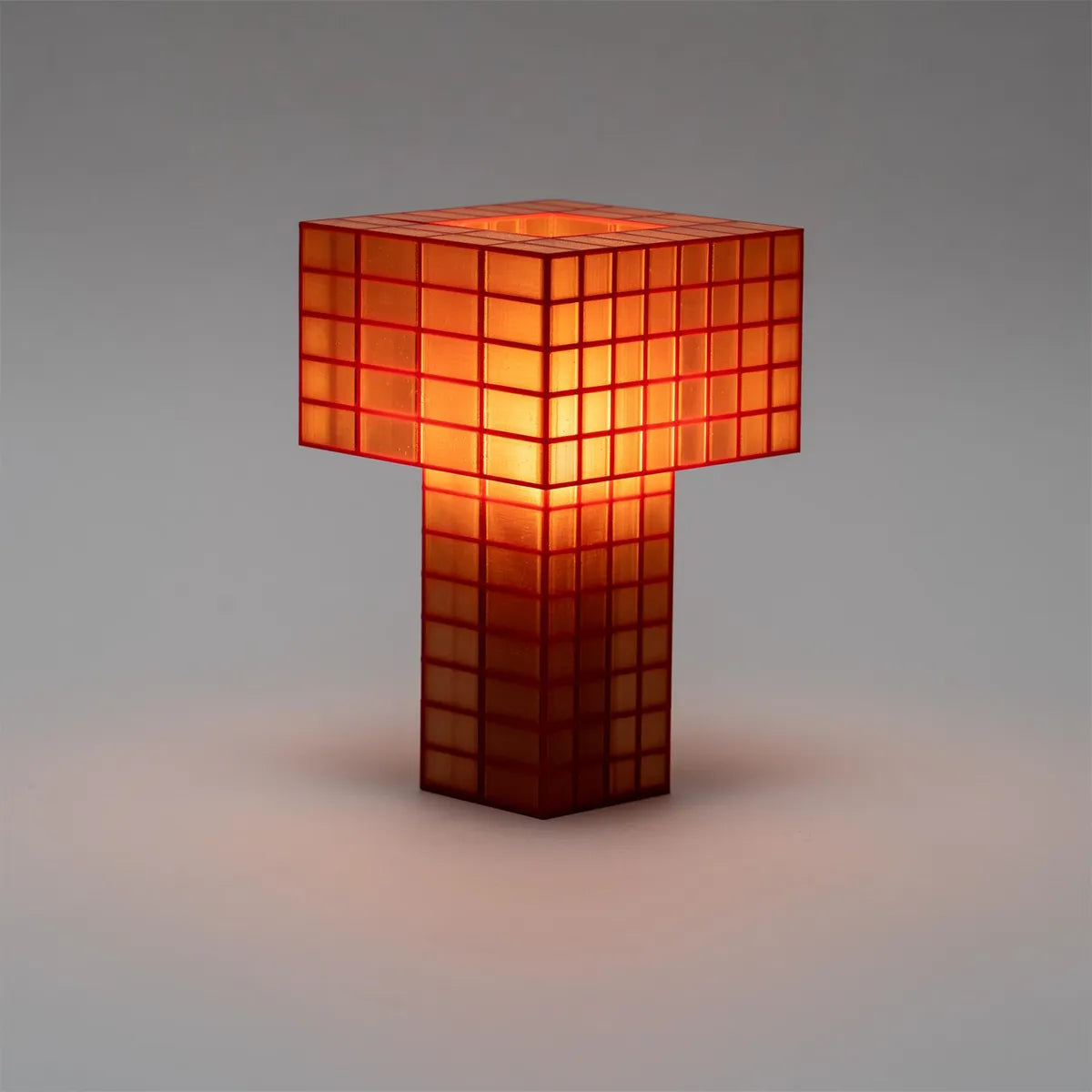 A Ridezign Tesser 5:8 table lamp shaped like a stylized letter T, constructed from glowing orange-red translucent square panels, set against a neutral gray background.