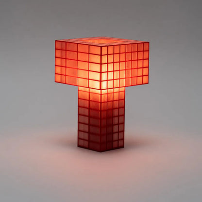 Illuminated Ridezign Tesser 5:8 table lamp in Cherry with an open top, made from a red grid over warm orange panels, casting a soft glow against a neutral grey-brown background.
