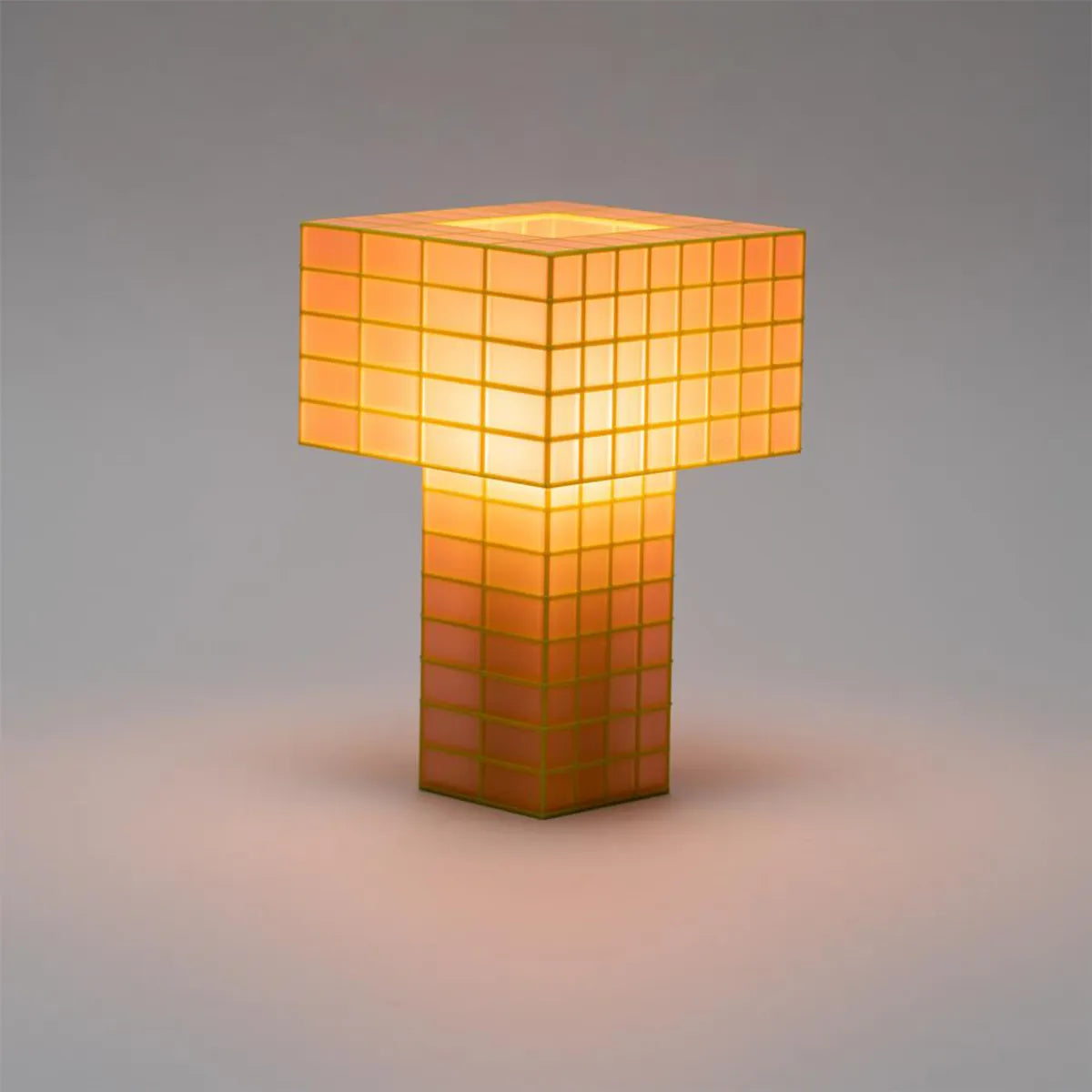 A Ridezign Tesser 5:8 table lamp with a glowing orange and yellow geometric grid design, set against a neutral gray background.