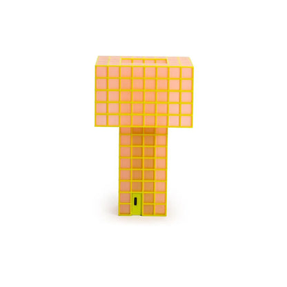 A Ridezign Tesser 5:8 Lamp with a grid pattern, featuring a bright yellow-orange body, a glowing warm pink-orange light panel on the top block, and a small lime green door at the base, set against a plain white background.