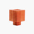 A translucent orange-red Ridezign Tesser 8:3 Lamp with a grid pattern, shaped like a stylized cube with a stepped base, shown on a plain white background.