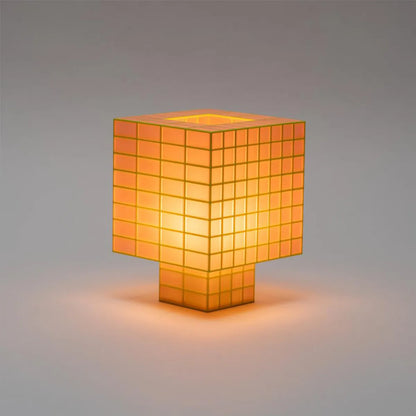 A Ridezign Tesser 8:3 table lamp with a cube-shaped shade and matching base, made of glowing warm orange translucent square panels, set against a neutral gray background.