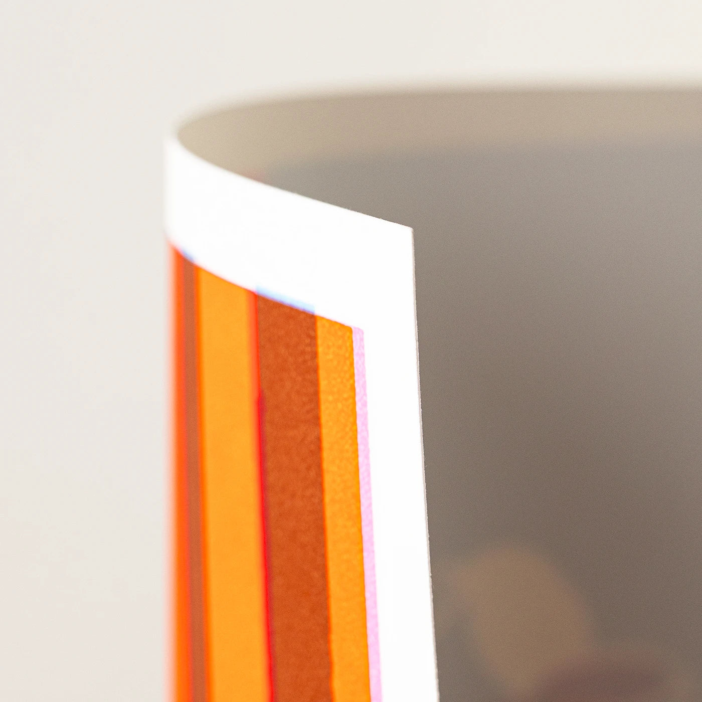 Close-up of an art print showing vertical orange and red stripes with a white edge, photographed against a light neutral background.