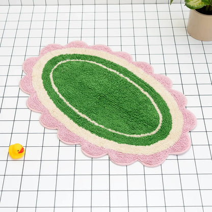 Green bath mat with pink and white scalloped edge on a grid background