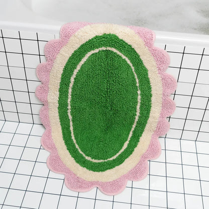 Decorative bath mat with green center, pink border, and scalloped edge on a grid background.