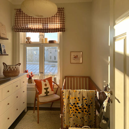 Nursery with checkered curtain, crib, and decorative items. A blanket with a tiger animal design hangs over the cot. 