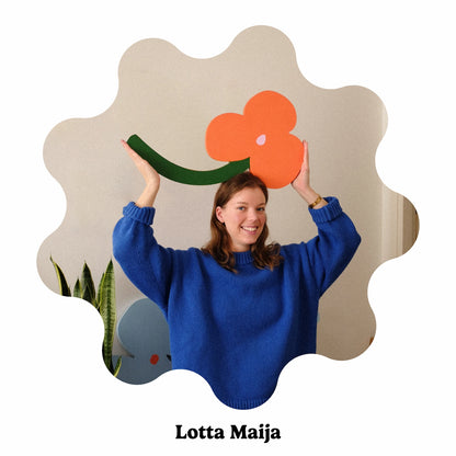 Portrait of Finland-based artist Lotta Maija wearing a bright blue knit sweater holds up a large orange flower decoration with a green stem. The photo is framed inside a wavy scalloped beige shape, with the text &